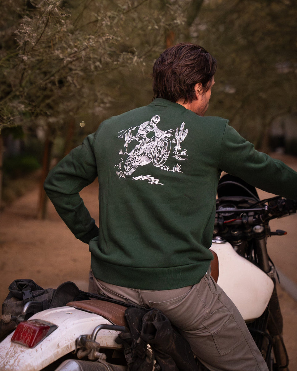 Model wearing Bike Shed Moto Desert Race Embroidered sweatshirt with a motorcycle in a dusty area