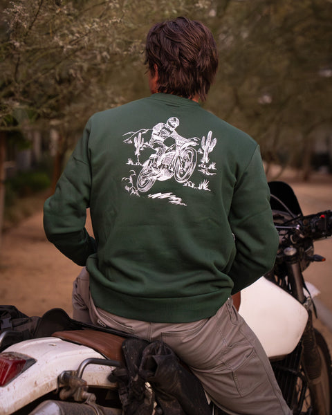 Model wearing Bike Shed Moto Desert Race Embroidered sweatshirt with a motorcycle in a dusty area