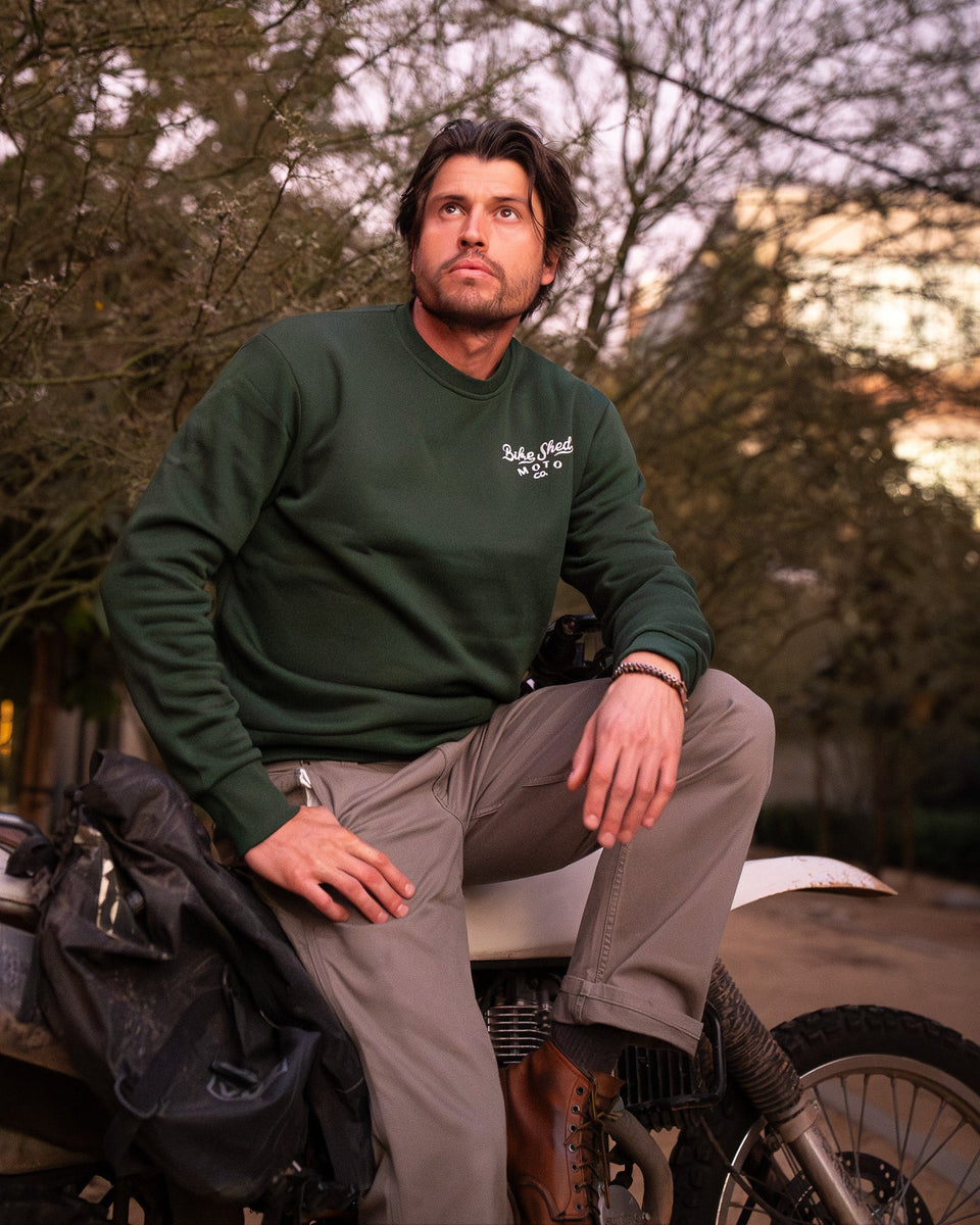 Model wearing Bike Shed Moto Desert Race Embroidered sweatshirt with a motorcycle in a dusty area