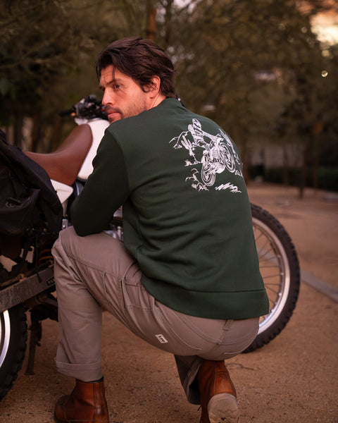 Model wearing Bike Shed Moto Desert Race Embroidered sweatshirt with a motorcycle in a dusty area