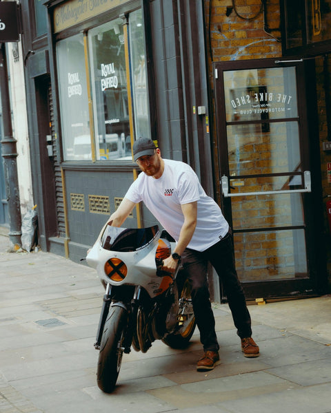 Model wearing Bike Shed Motorcycle Race T-Shirt White next to a custom motorcycle.